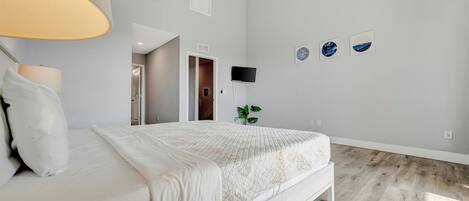 A bedroom with a bed, a lamp, a TV, and a plant.