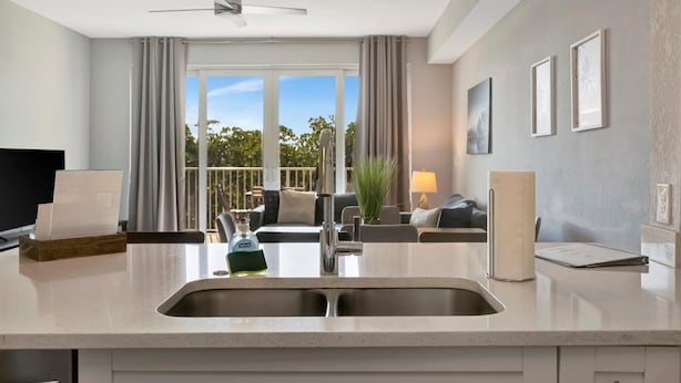 A modern kitchen with a built-in sink, a ceiling fan, and a view of the outdoors through large windows. - Mangrove Point Townhome (Ruskin)