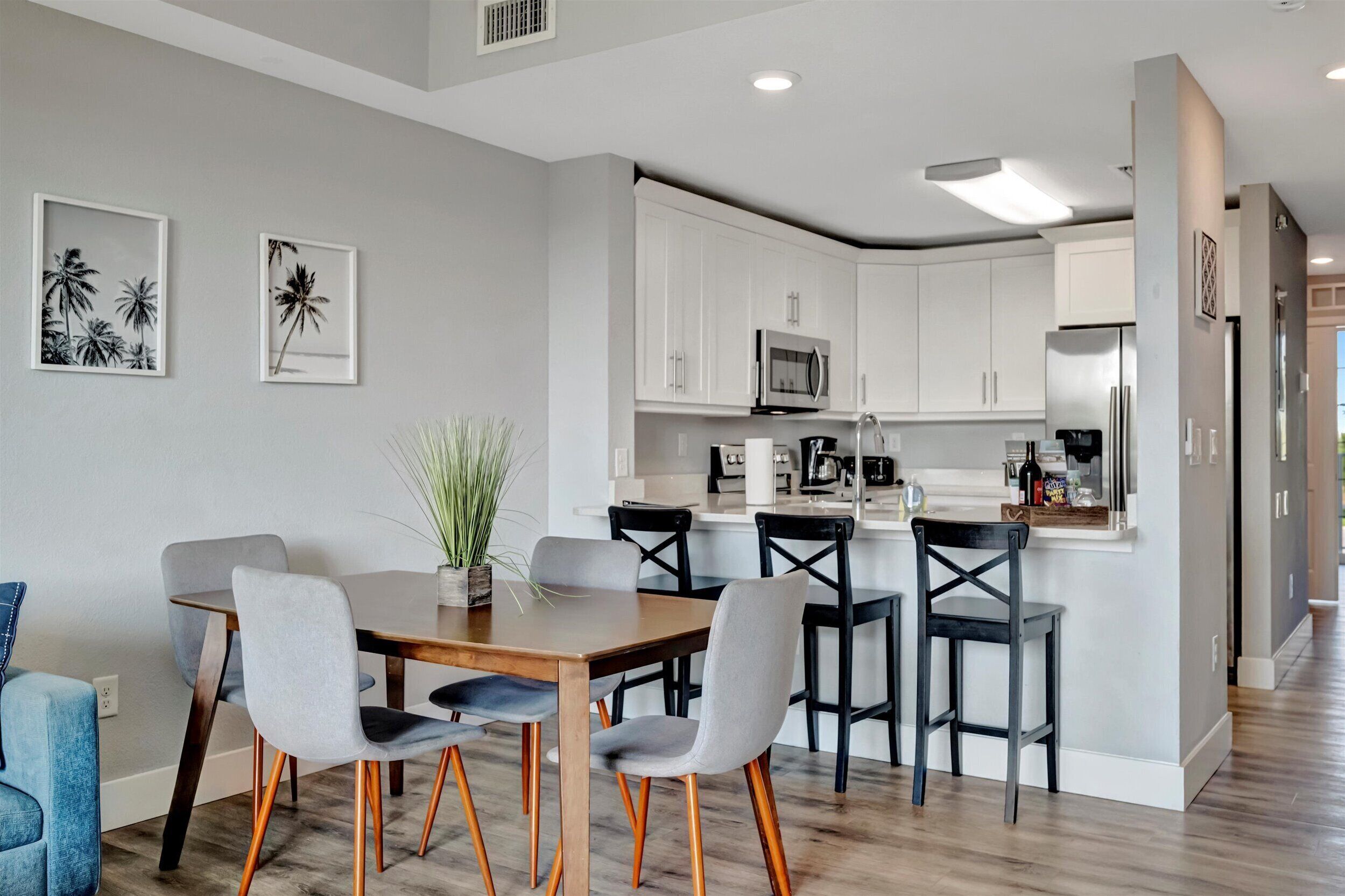 A modern kitchen with white cabinets, a microwave, and a refrigerator. There is a dining area with a wooden table and chairs.