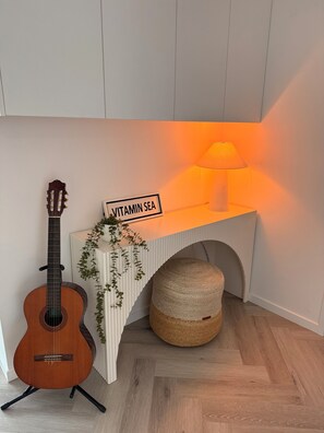 A guitar, a sign reading 'VITAMIN SEA,' a lamp, and a woven basket in a room with wooden flooring and white walls. - Waterfront Gold Coast Luxury apartment on the Lagoon (Labrador)