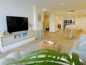 A modern living room with a flat-screen TV, a sofa, a coffee table, and a dining area with a table and chairs. - Waterfront Gold Coast Luxury apartment on the Lagoon (Labrador)