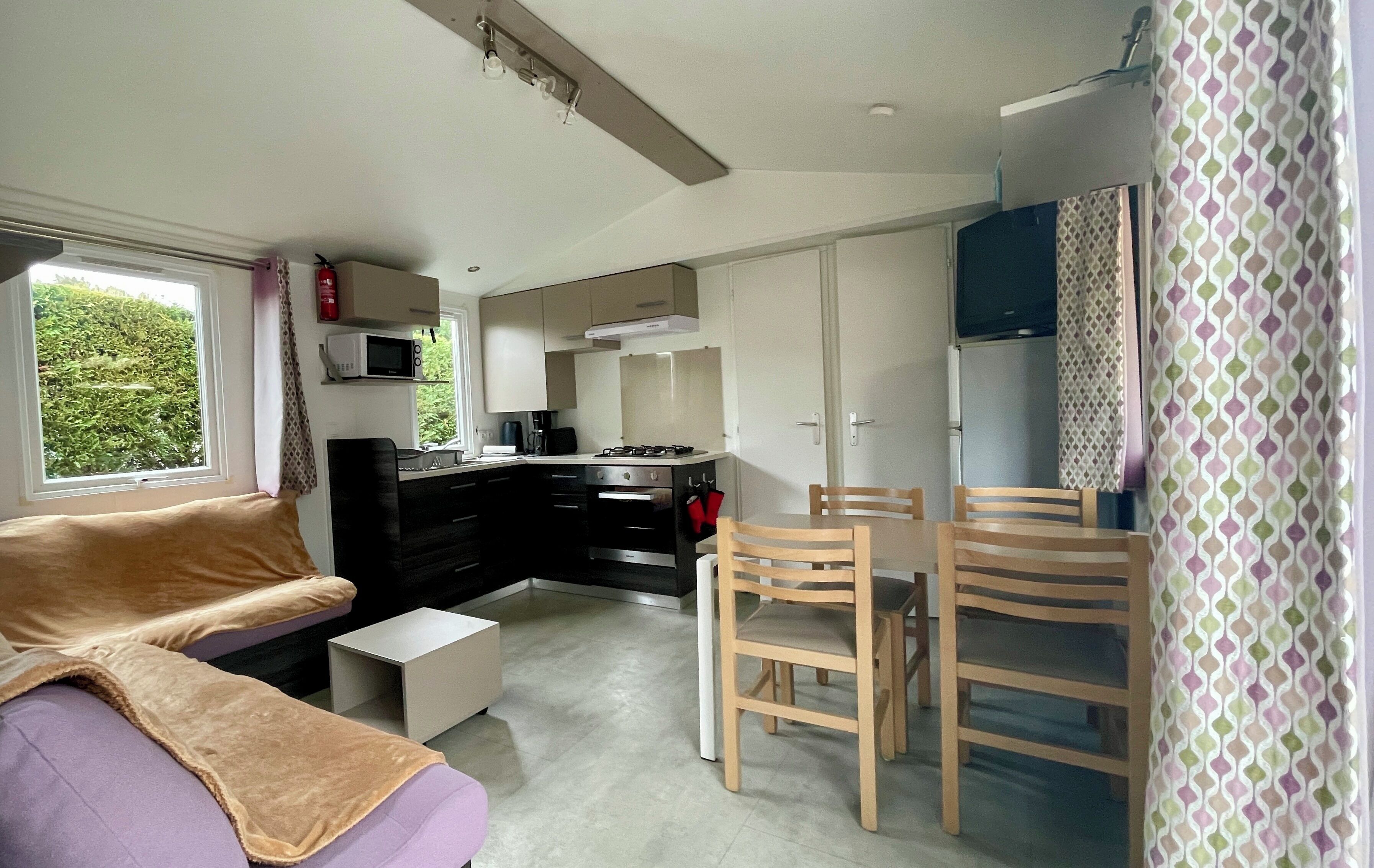 Un espace de vie compact comprenant un coin cuisine, un canapé, une table à manger avec des chaises et une fenêtre avec des rideaux.