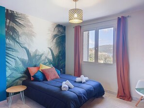Una camera da letto con un letto grande, un tavolino, una finestra con tende e un affresco al muro.