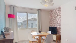 Ein modernes Zimmer mit Esstisch, Stühlen, einem Fernseher und einem großen Fenster mit Blick auf Gebäude.
