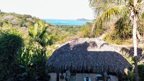 A patio with a thatched roof, outdoor furniture, and a view of the ocean. - CasaMyra American Gourmet Breakfast Included (Playa Panama, Papagyo Bay)