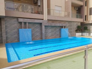 A swimming pool with a tiled deck, a marble wall, and a balcony with a railing. - Cozy apartment very close to the beach (Hammamet Sud)