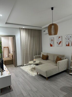 A modern living room with a sectional sofa, a small round coffee table, and a pendant light. - Cozy apartment very close to the beach (Hammamet Sud)