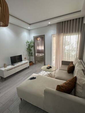 A modern living room with a sofa, TV, and a small table with a candle. - Cozy apartment very close to the beach (Hammamet Sud)