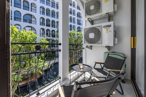 A balcony with a view of a building, two air conditioning units, a small table with a candle, and a chair. - Harmony by TropicLook | Pool & Gym Access | Rawai (Rawai)