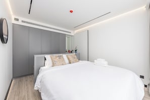 A modern hotel room with a large bed, a radiator, a mirror, and a wall-mounted clock. - Harmony by TropicLook | Pool & Gym Access | Rawai (Rawai)