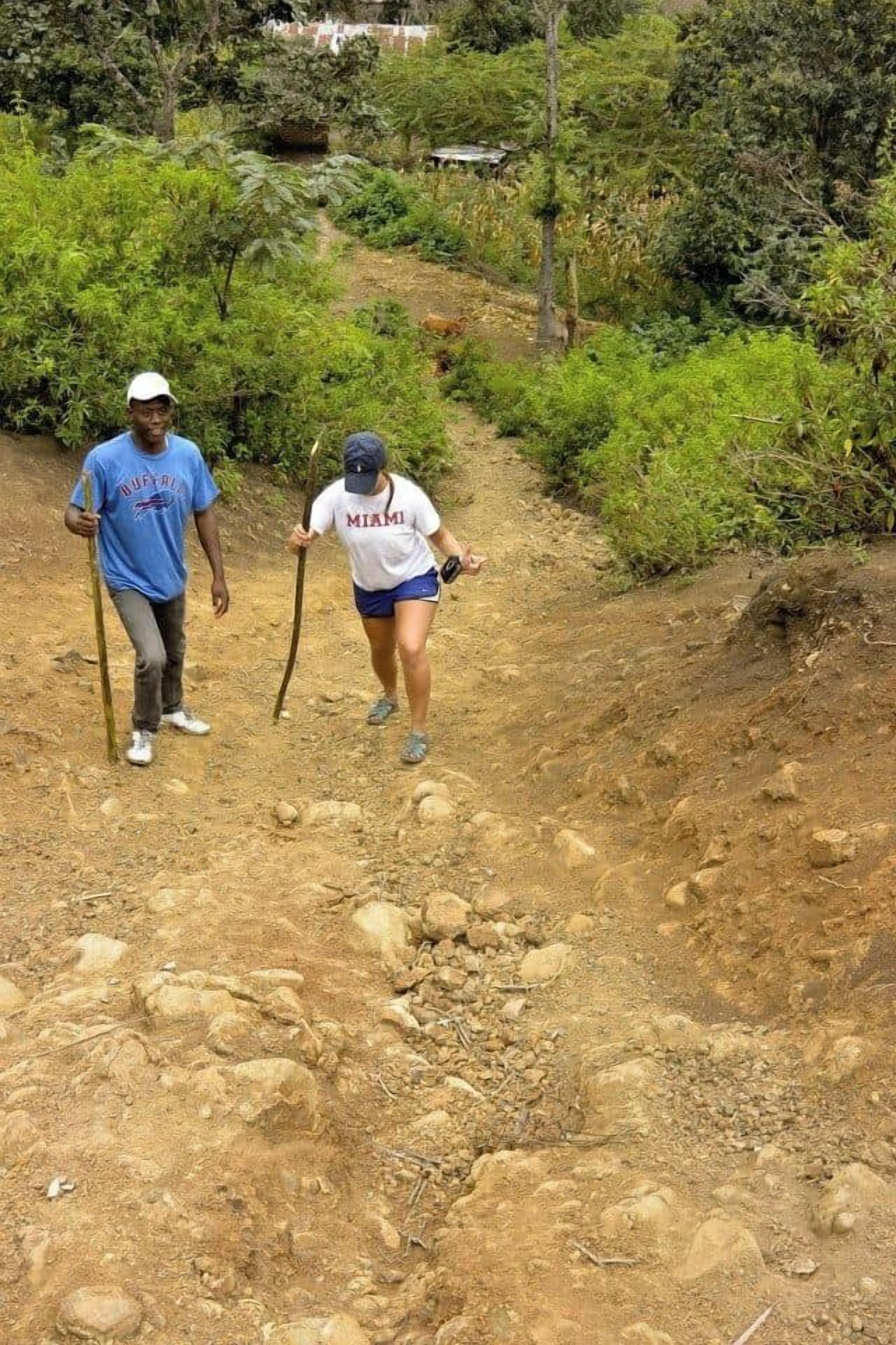 Two people hiking on a dirt path surrounded by greenery.