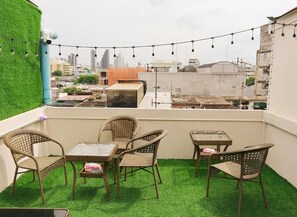 A rooftop terrace with artificial grass, wicker furniture, and string lights.