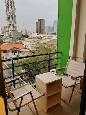 A balcony with a view of a cityscape, including tall buildings and a green screen. - Holy Hostel Sathorn (Bangkok)