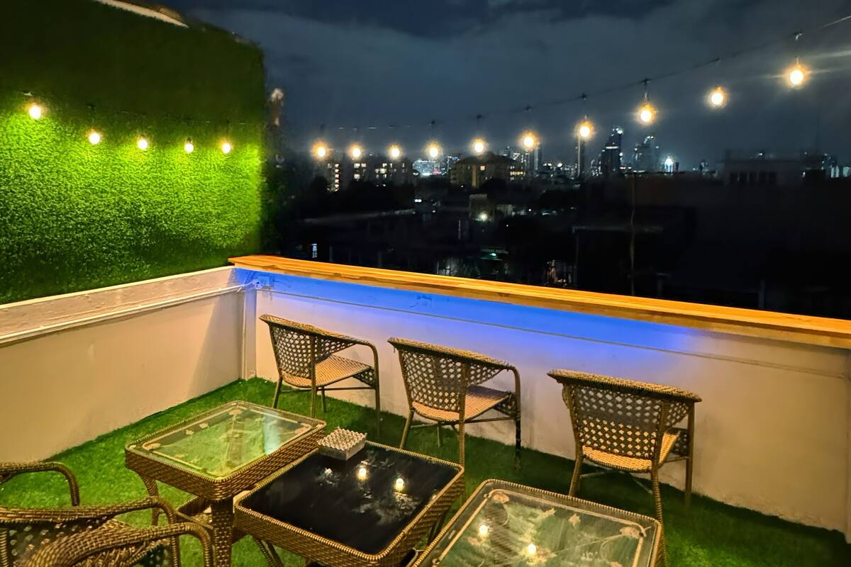 A rooftop terrace with wicker furniture and a green wall, overlooking a cityscape at night.
