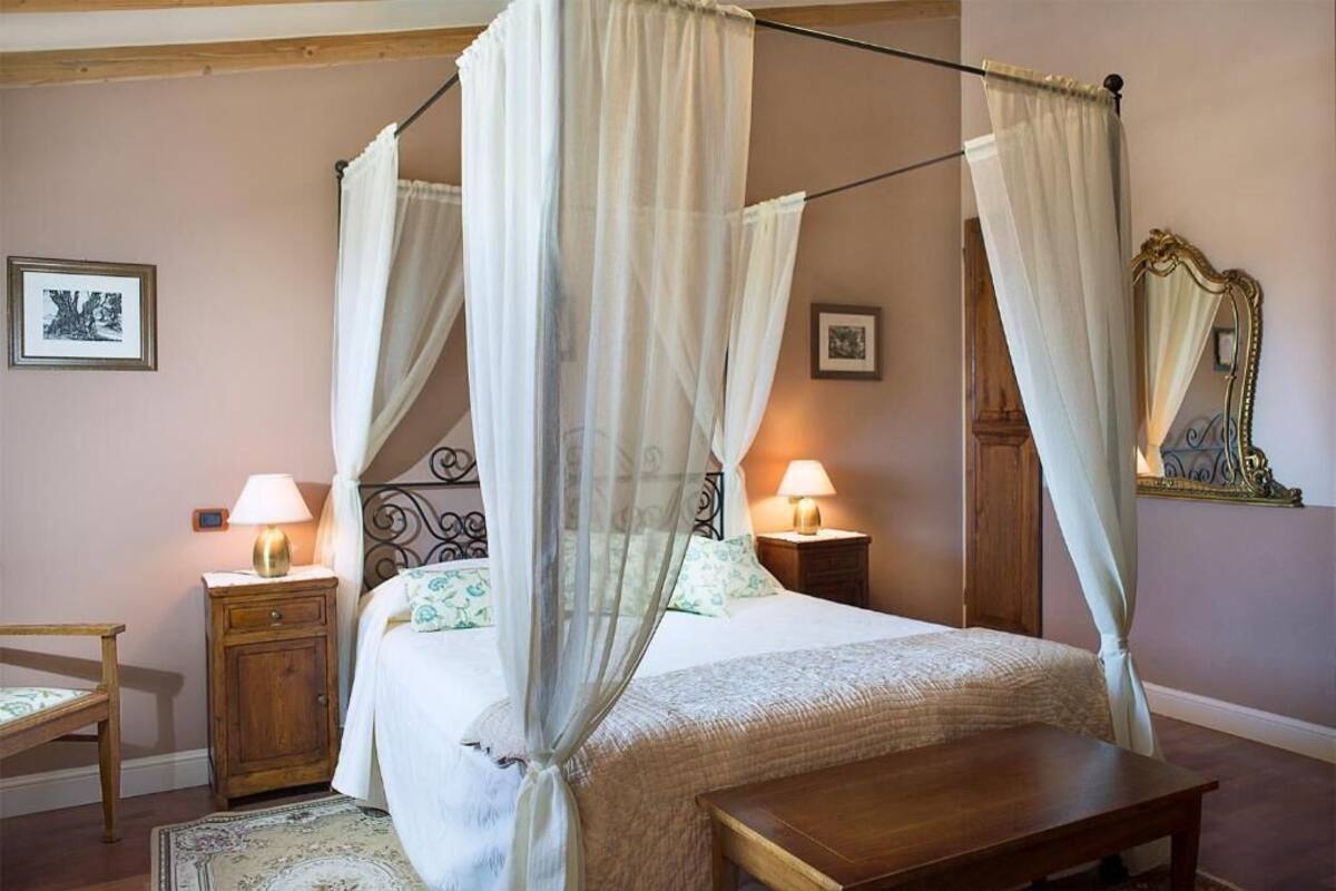 A bedroom with a four-poster bed, two bedside lamps, a wooden nightstand, a chair, and a mirror on the wall.