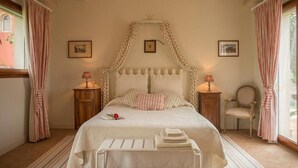 A bedroom with a canopy bed, two bedside tables with lamps, a chair, and a window with curtains. - L'ANTIGO GRANARO (Ancona)