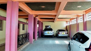 Een parkeergarage met roze en gele muren, twee auto's staan er geparkeerd, en een zwarte reling.