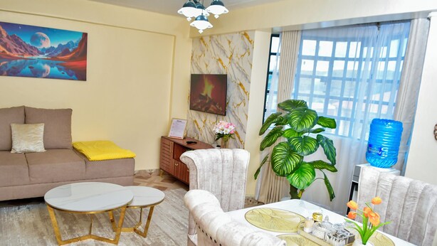 Een woonkamer met een bank, twee ronde tafels, een eettafel met stoelen, een grote plant en kunstwerken aan de wanden.