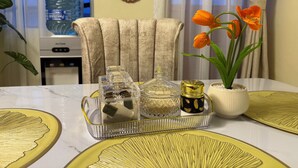 Een eetgedeelte met een tafel voor twee personen, voorzien van een waterdispenser, een stoel en decoratieve items, waaronder een vaas met bloemen.