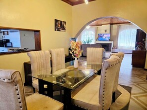 A dining area with a glass-top table, cushioned chairs, a vase with flowers, and a kitchen in the background. - Beautiful 4 bedroom home located in the heart of Naivasha town. (Naivasha)