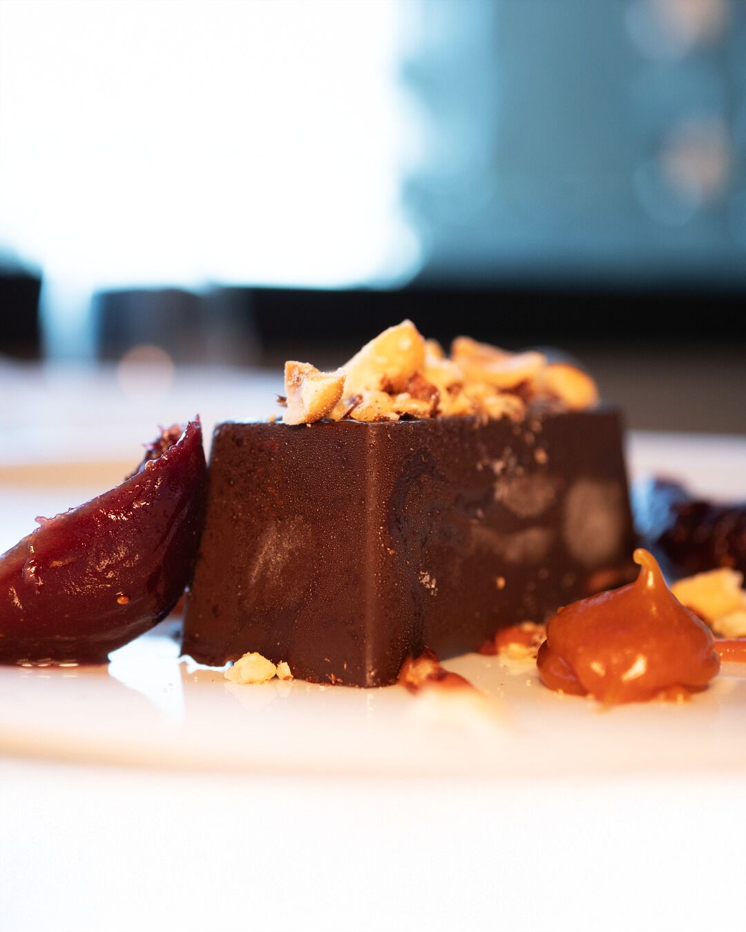 A dessert with a dark chocolate base, garnished with nuts and fruit pieces.