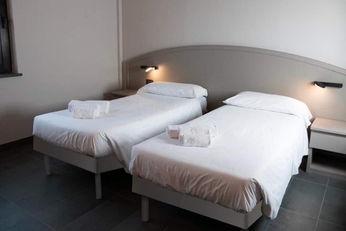 A double room with two beds, each with a pillow and a towel, and bedside lamps.
