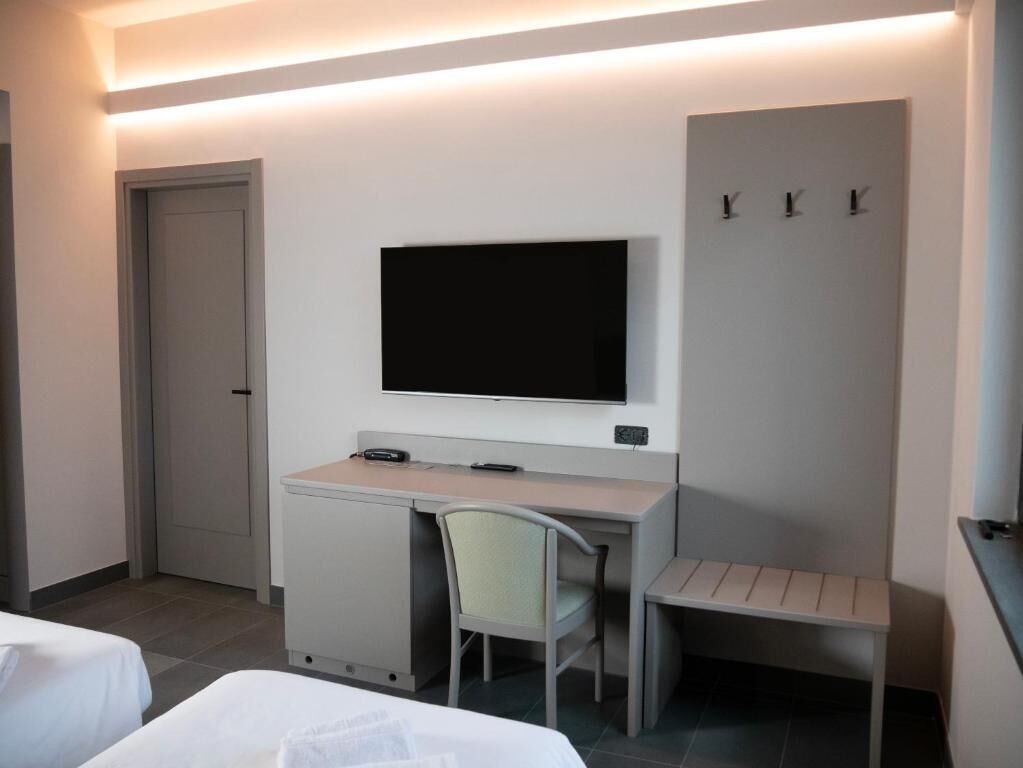 Una habitación de hotel con cama, escritorio, silla, televisor y armario.