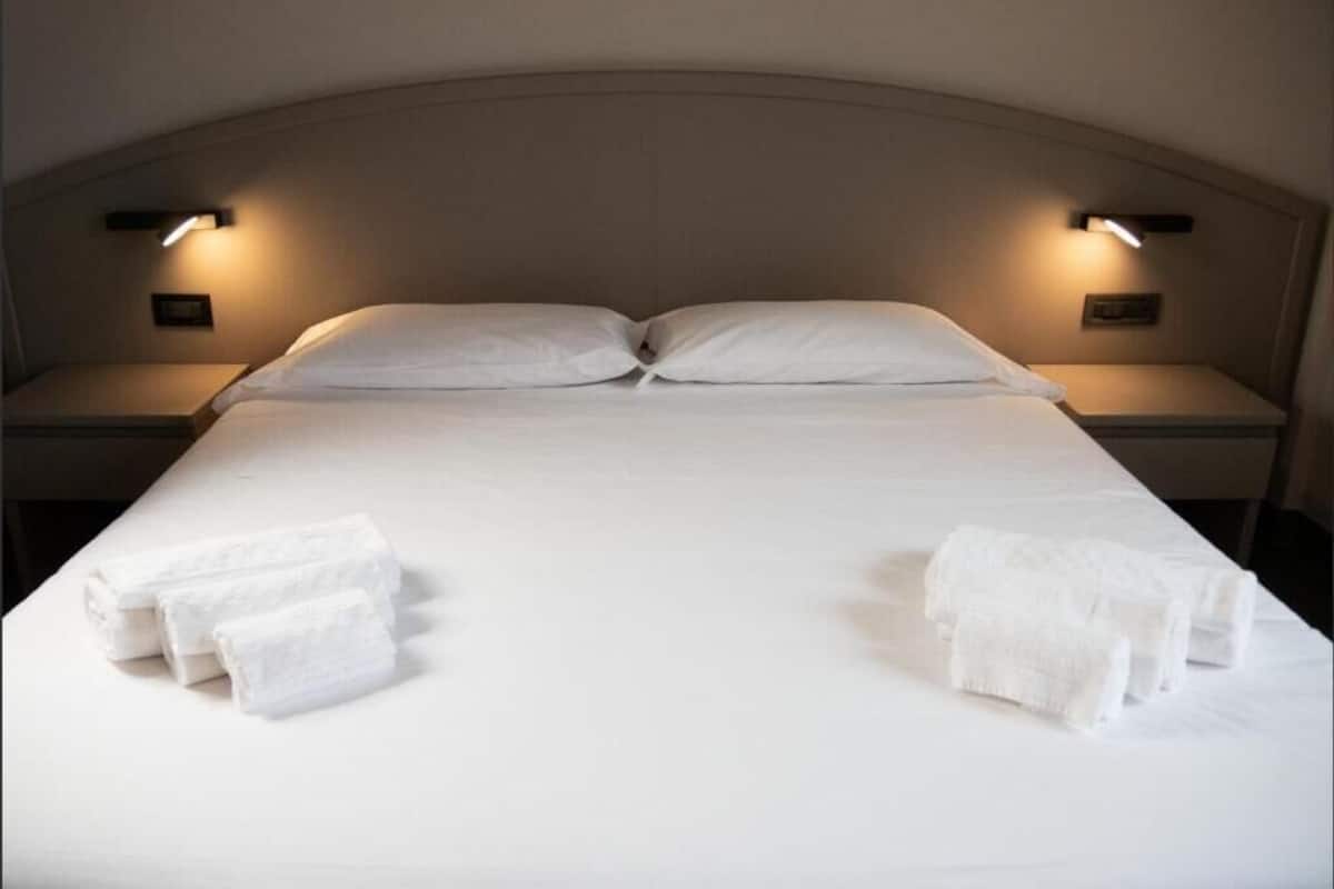 A neatly made bed with white linens and towels, two bedside lamps, and a headboard.