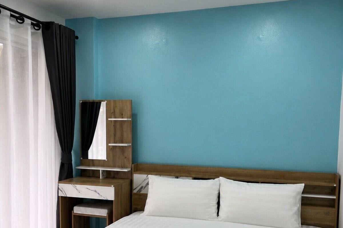Ein Hotelzimmer mit einem Bett, einem Nachttisch aus Holz, einem Spiegel und einem Fenster mit Vorhängen.