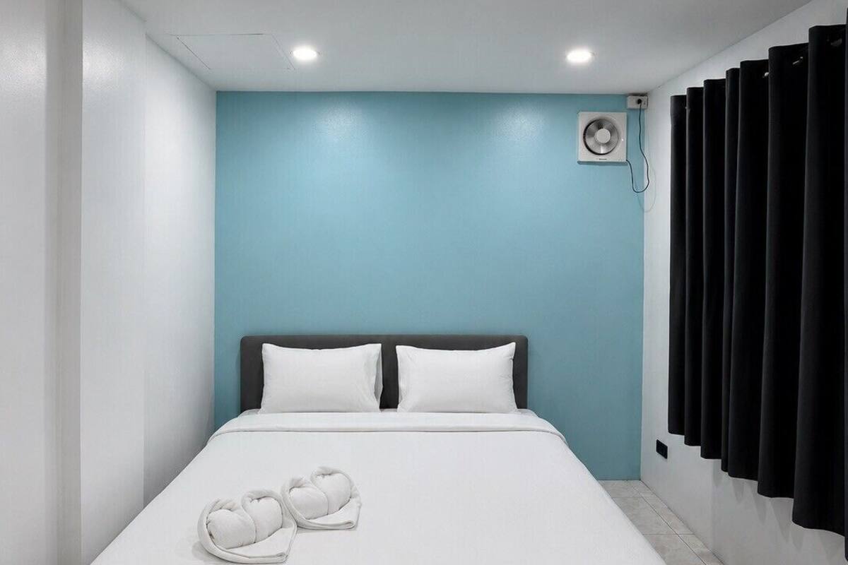 Ein modernes Hotelzimmer mit einem großen Bett, einem Deckenventilator und schwarzen Vorhängen.