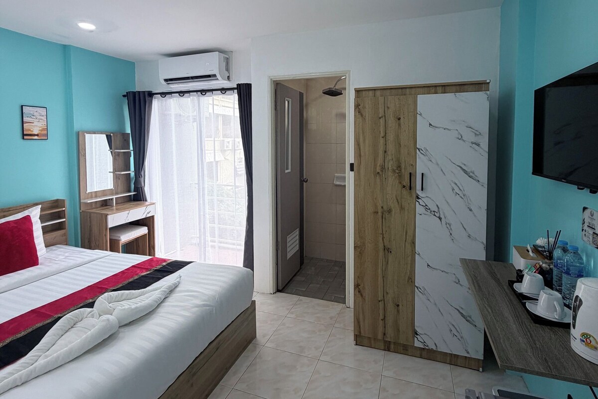 A hotel room with a bed, a desk, a TV, and a shower area.