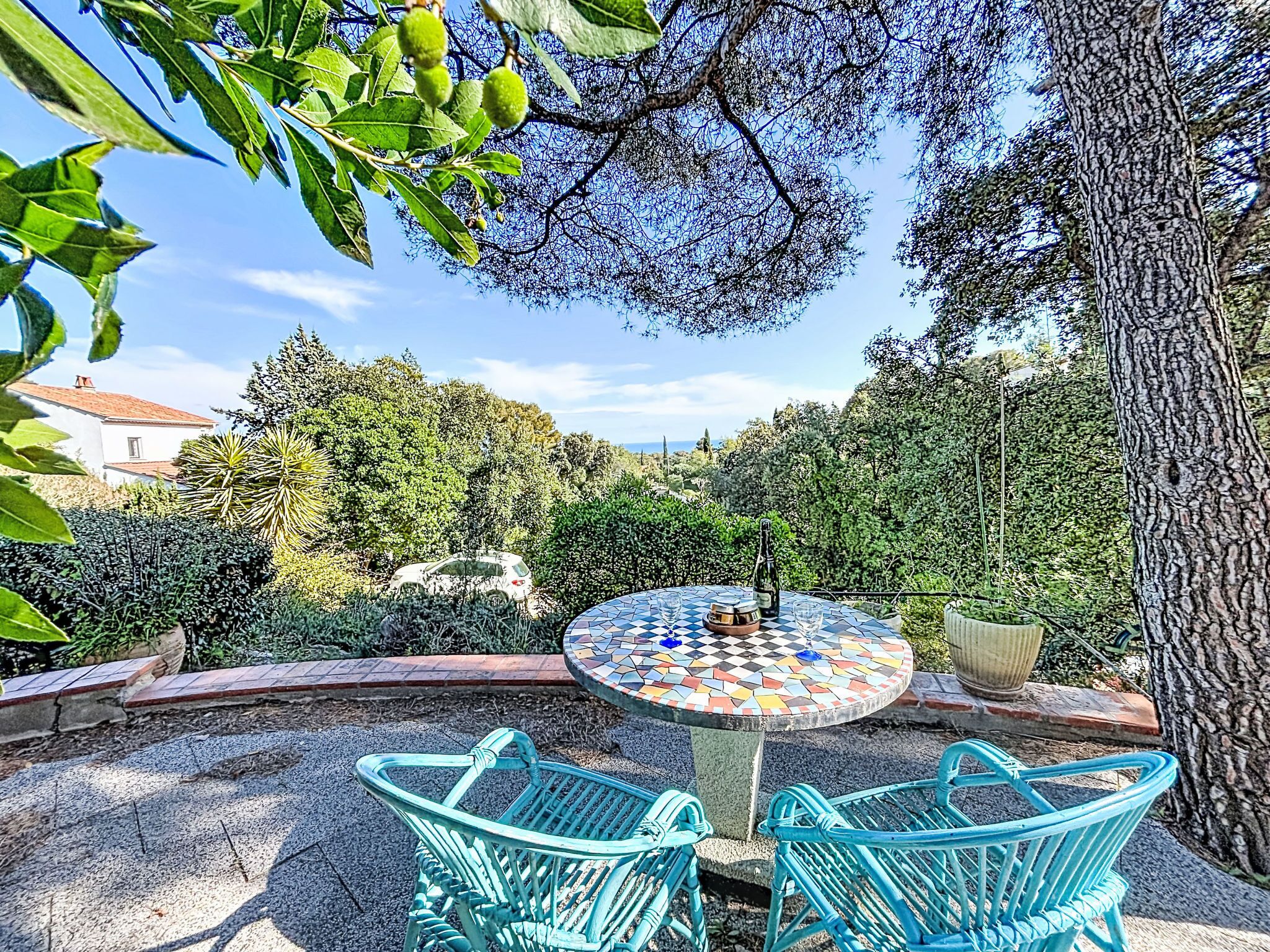 A garden patio with a mosaic table, two chairs, and a bottle of wine.