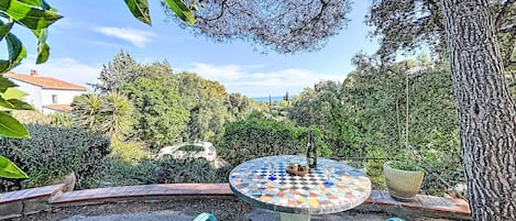 Een tuinpatio met een mozaiektafel, twee stoelen en een fles wijn.