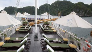 A deck with rows of sun loungers, umbrellas, and tables, overlooking a body of water with hills in the background. - LAN HA BAY  STAR CRUISE  (Tuan Chau)