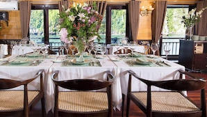 A dining area with tables set for four, each with a vase of flowers, and a view of a natural landscape through large windows. - LAN HA BAY  STAR CRUISE  (Tuan Chau)