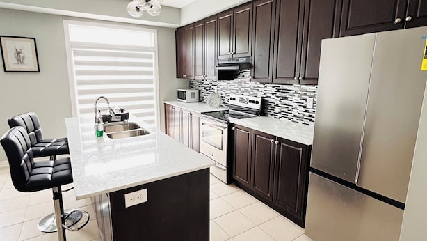 A modern kitchen with dark cabinets, a stainless steel refrigerator, a microwave, and a large island with stools.