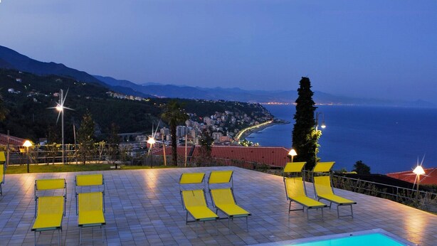 A pool area with sun loungers and a view of the sea at dusk. - Apartment in Cogoleto with pool (Cogoleto)