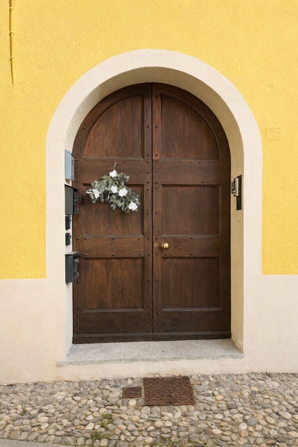 A double wooden door with a white archway, a small flower arrangement, and a manhole cover on a stone-paved ground.