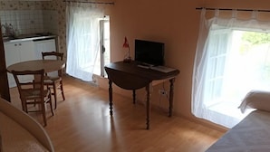 Quarto com mesa de jantar de madeira, televisão, área de cozinha com pia e janela com cortinas.