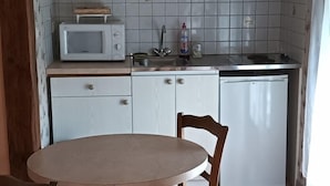 Cozinha equipada com micro-ondas, pia e máquina de lavar louça. Há uma mesa redonda e uma cadeira.