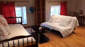 Une pièce comprenant un lit, un canapé blanc, une petite table, un lampadaire et une fenêtre avec des rideaux rouges.