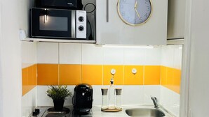 Eine kompakte Küche mit Mikrowelle, einer Bosch-Kaffeemaschine, Spüle und einer Wanduhr.