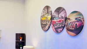 Un salón con un sofá azul, una lámpara y tres cuadros con imágenes de coches antiguos.