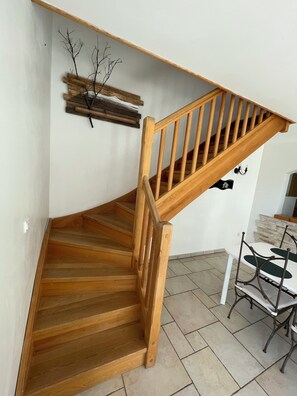 A wooden staircase with a handrail, a dining table with chairs, and a wall-mounted light fixture.