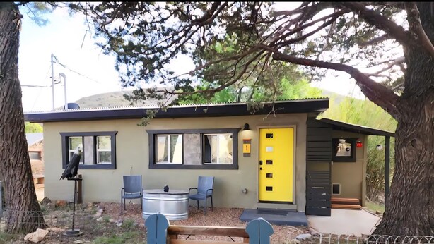 A small building with a yellow door, two windows, and a bench outside. -  The Bisbee Vista Cabin, Cozy Desert Retreat + Mountain Views (Bisbee)