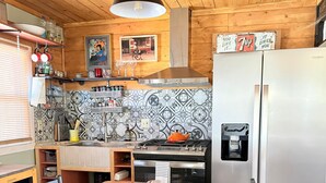 A wooden interior with a dining table, chairs, a refrigerator, and a kitchen area with a patterned backsplash. -  The Bisbee Vista Cabin, Cozy Desert Retreat + Mountain Views (Bisbee)