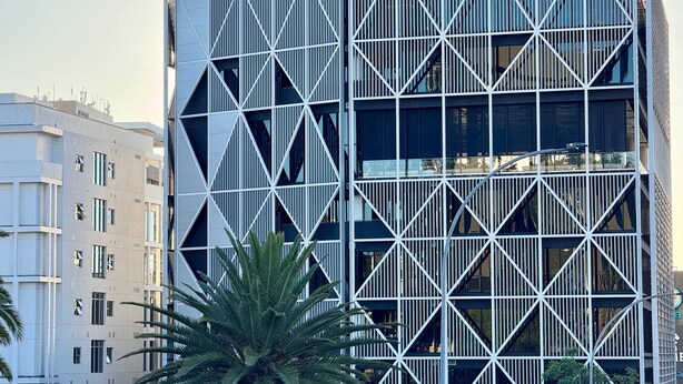 Un edificio moderno con fachada geométrica, varios pisos y una entrada destacada.
