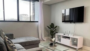 Una sala de estar moderna con un sofá, una mesa de centro de vidrio, un televisor en la pared y un ventanal grande.