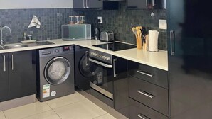 Una cocina moderna con armarios oscuros, horno empotrado, microondas y lavadora.