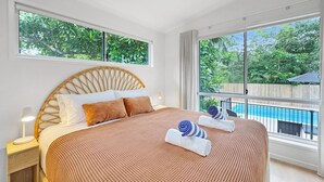 Een slaapkamer met een groot bed, nachtkastje, raam met uitzicht op een zwembad en een balkon.